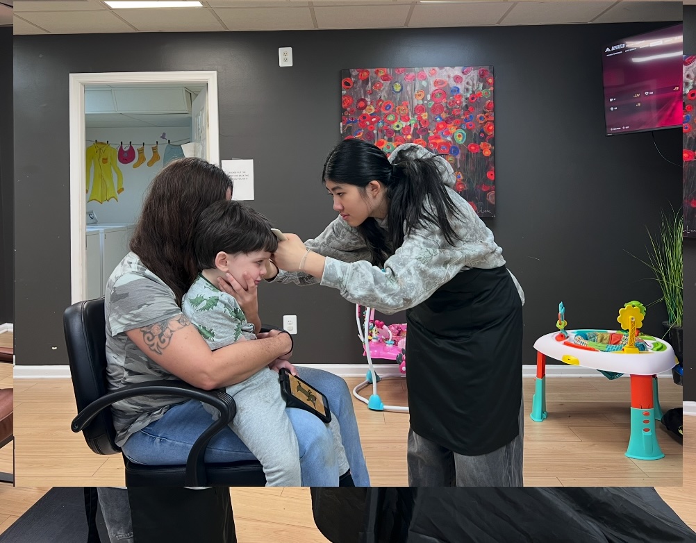 Ava trimming a child's hair with support from his mother
