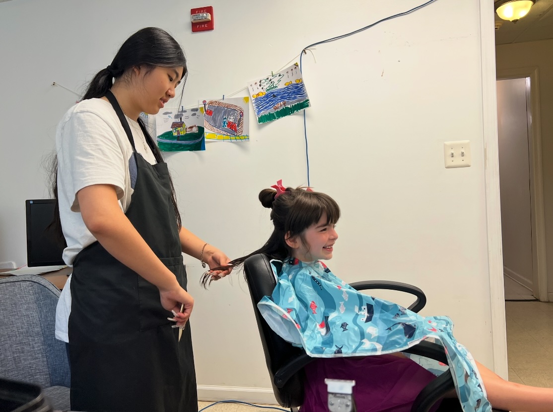 Ava cutting a young girl's hair during a community session