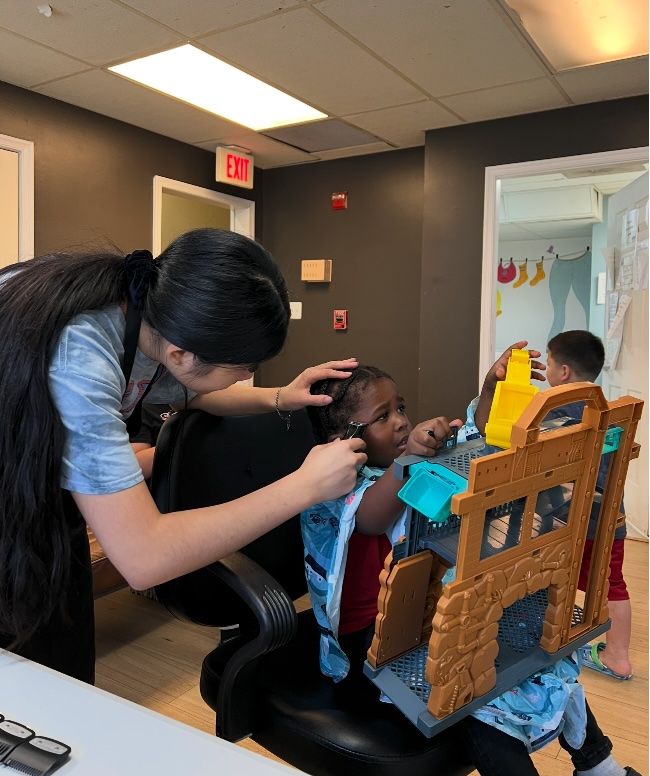 Ava carefully cutting a young girl's hair as she plays